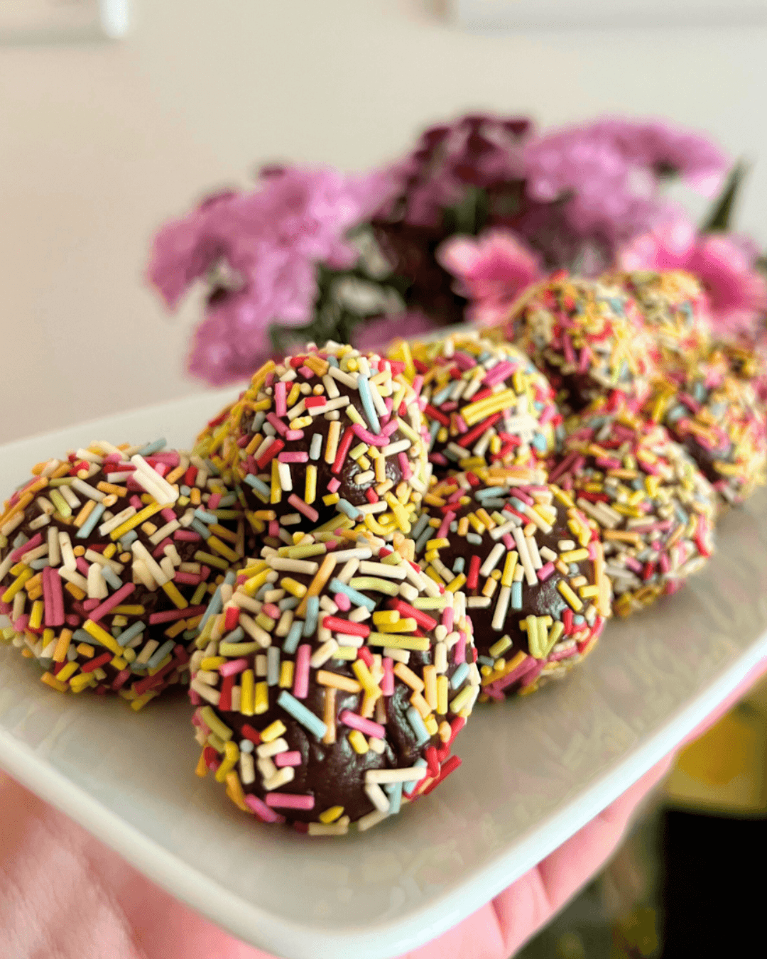 A plate of round chocolate brigadeiro truffles coated in colourful rainbow sprinkles.