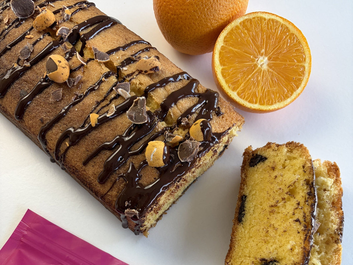A sliced chocolate chip orange loaf cake drizzled with chocolate, served with a fresh orange.