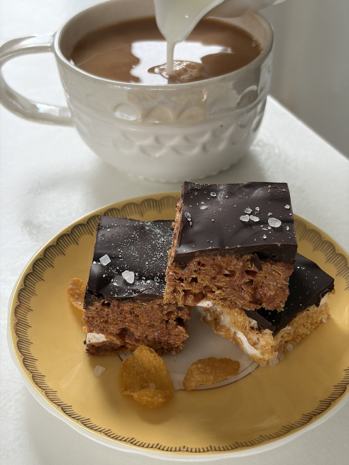 Three cornflake and marshmallow squares topped with chocolate, arranged on a white plate.