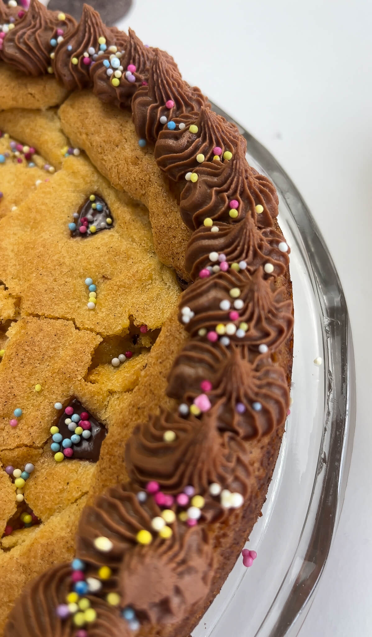 An overhead view of a deep-dish chocolate chip cookie decorated with piped chocolate buttercream and sprinkles.
