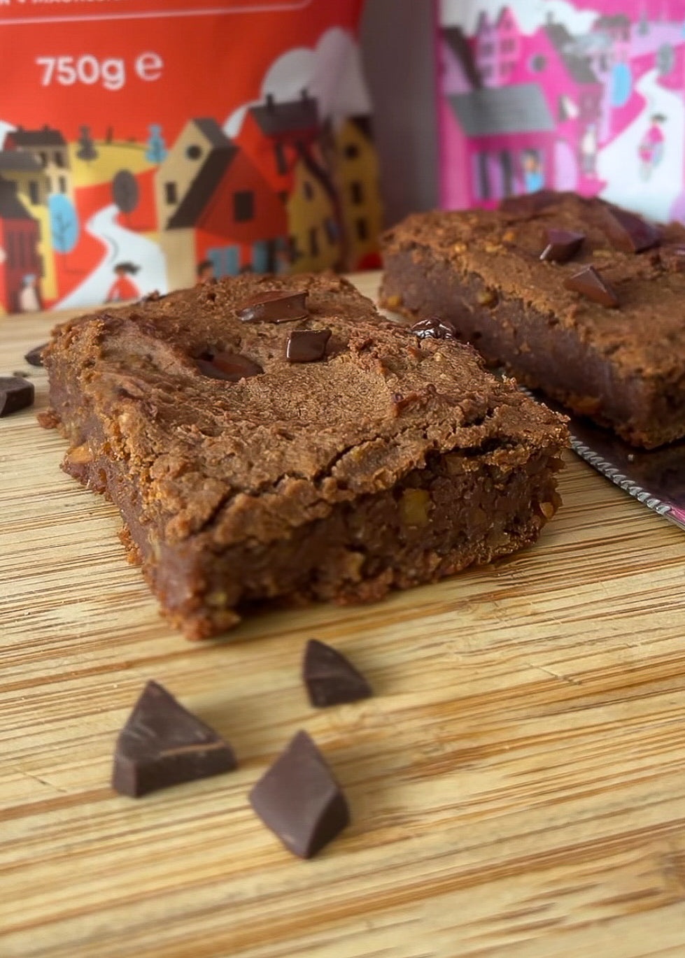 Chickpea brownie squares on a wooden board next to bags of Food Thoughts Organic Cacao Powder and 70% Dark Chocolate Chips.