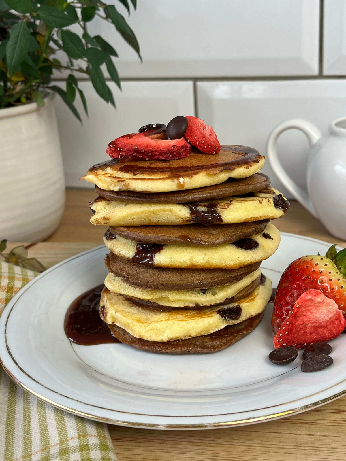 A stack of pancakes topped with strawberries and drizzled with chocolate sauce.